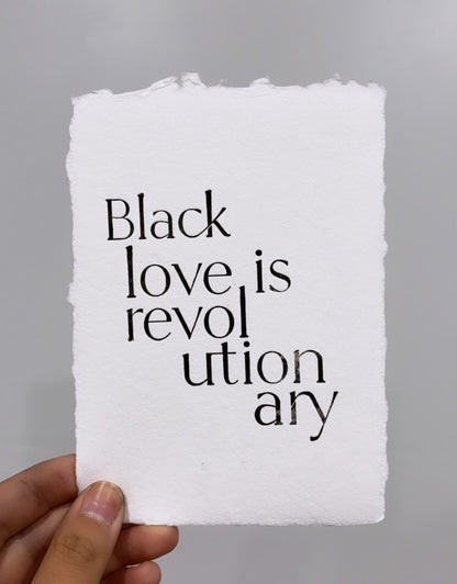 white piece of handmade paper being held by hand reads "Black love is revolutionary"